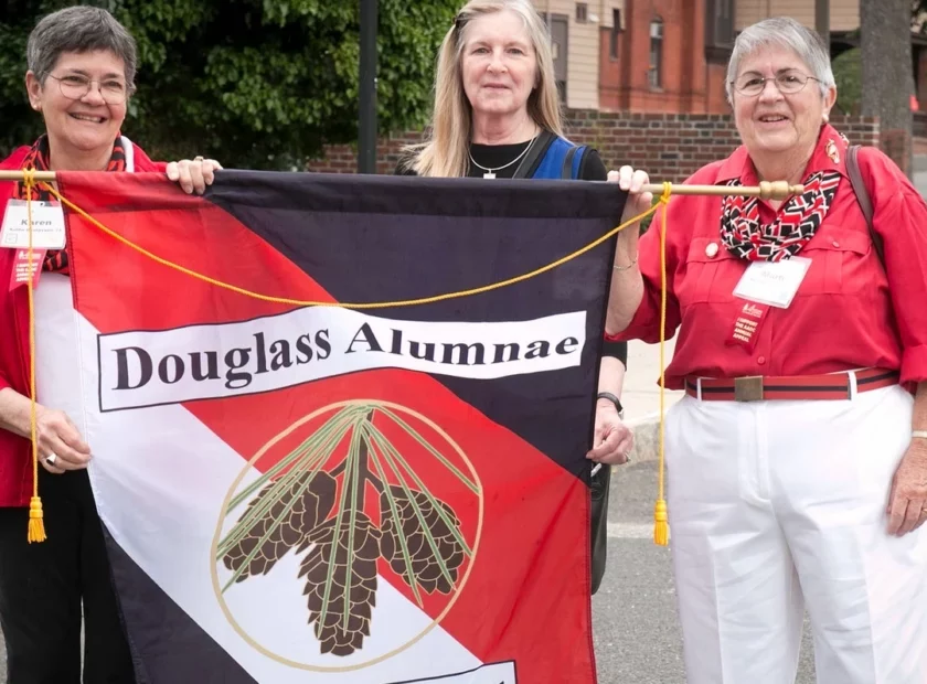 Three Douglass Alumnae hold a Douglass Alumnae Banner