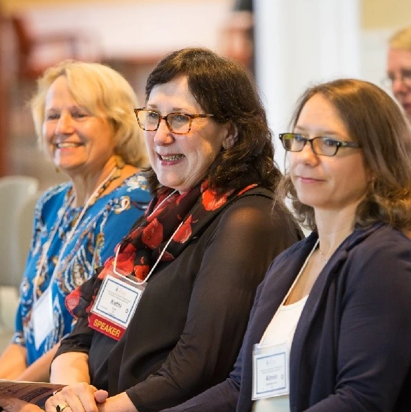 Three women smiling in the audience at a mentoring event sponsored by the AADC